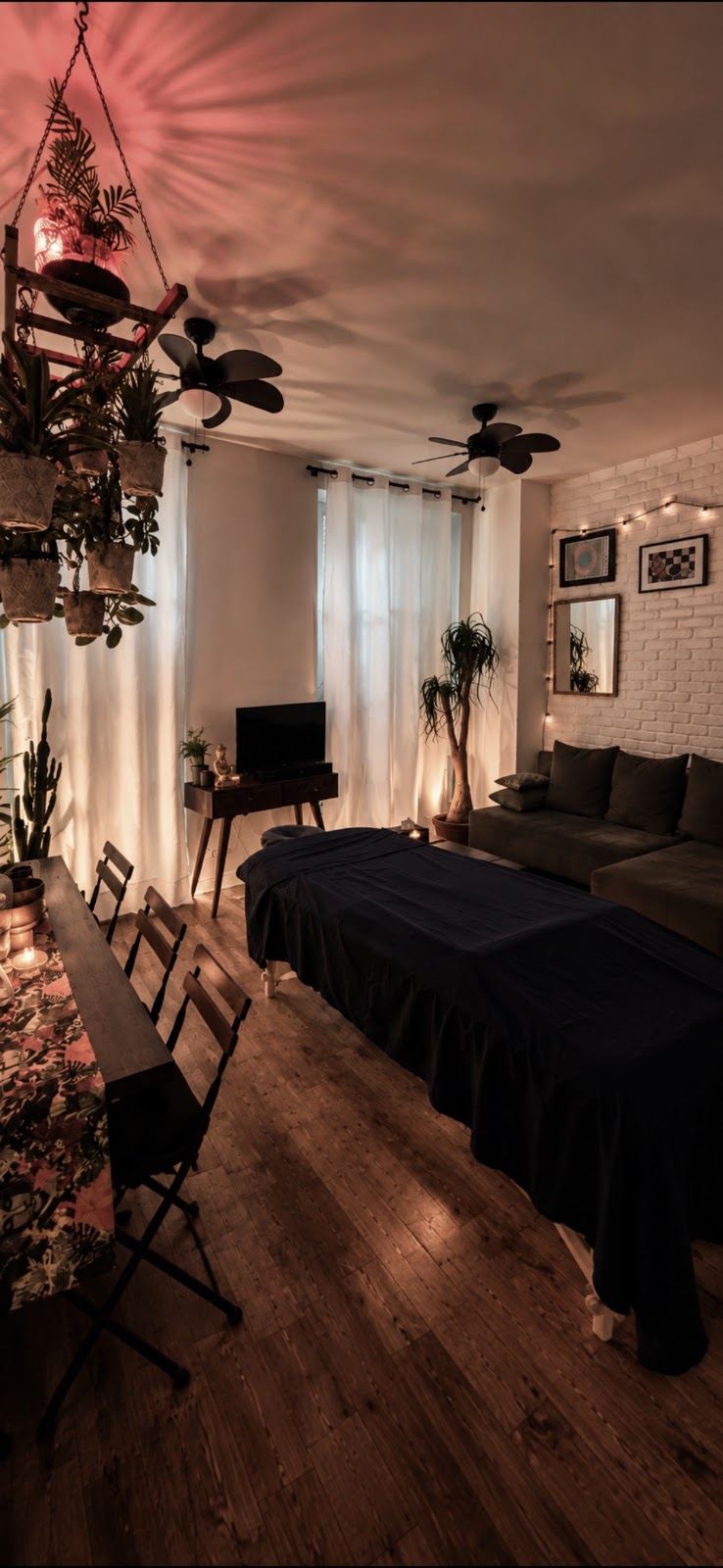Le salon de massage le soir : table drapée de bleu nuit, bougies, plantes suspendues et ombres de feuilles au plafond